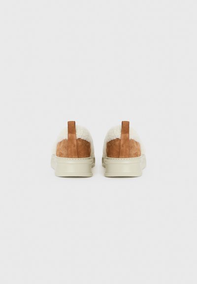 Brown suede shoes with cream shearling accents and a beige rubber sole, featuring a small heel tab for easy wearing.