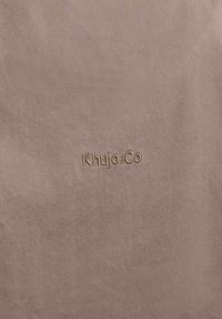 Beež kangas peent diagonaalset tekstuuri, millel on tikitud Khrujo&Co logo sama värvi niidiga.