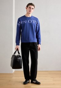 Sudadera azul con el logo blanco de "Marc O’Polo", pantalones negros, bolso negro y zapatillas negras con rayas blancas. Diseño simple y corte relajado.
