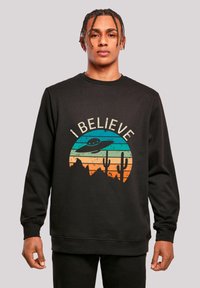 Schwarzer Pullover mit einem Grafikdesign, das ein UFO, Berge und Kakteen auf horizontalen Verlaufstreifen in Blau, Orange und Gelb zeigt.