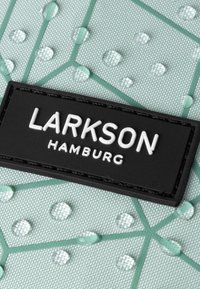Tessuto di un blu chiaro textured con gocce d'acqua in rilievo e una patch rettangolare nera con la scritta "LARKSON HAMBURG" in lettere bianche.