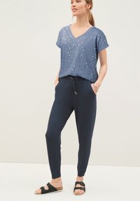 Camiseta azul con patrón de estrellas plateadas, escote en V y mangas enrolladas, combinada con pantalones jogger navy con cintura elástica y bolsillos. Sandalias negras.