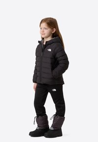 Crna puf jakna s kapuljačom i prednjim patentnim zatvaračem, crne hlače i topli čizmi. Svi predmeti imaju logotip The North Face.