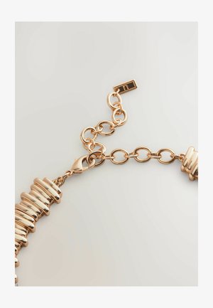 Kuldse tooniga kett-ranneke silindriliste metallhelmestega, varustatud lõksuklambri ja reguleeritavate linkidega. Sile, läikiv tekstuur.