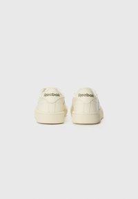 Kremfargede lær sneakers med flat såle, som har en teksturert gummisåle og embossert "Reebok"-logo på baksiden.