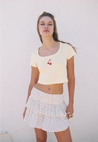 Gul kort t-shirt med rött körsbärsgrafik; kombinerad med en vit, volangprydd kjol med svarta prickar. Mjuka texturer.