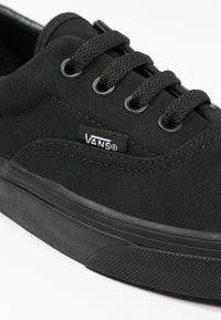 Schwarze Leinensneaker mit runder Zehenpartie, sechs Ösen, schwarzen Schnürsenkeln, Gummisohle und Vans-Logo an der Seite. Strukturierte schwarze Akzente.