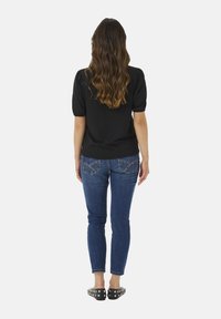 Black puff-sleeve top, blue skinny jeans with decorative back pockets, and black flats with studs, viewed from the back.