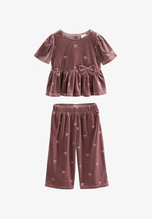 Sarkans divdaļīgs komplekts no samta, putekļu rozā krāsā. Augšdaļa ir pepluma stila ar īsām pūkām un priekšu ar loku; apakšdaļa ir īsa, ar loku rakstu.