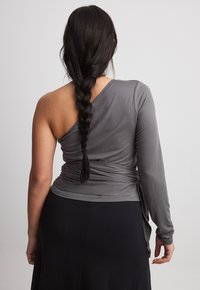 Haut asymétrique gris avec une manche longue, présentant un dos drapé et un tissu doux, associé à une jupe noire.