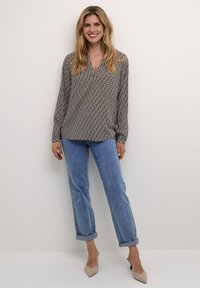 Blusa a maniche lunghe bianca e nera a fantasia con scollatura a V, abbinata a jeans in denim blu arrotolati e tacchi beige a punta.