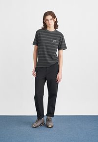 Černé a šedé pruhované tričko s kapsou na hrudi. Kombinováno s volnými černými kalhotami a šedými turistickými botami s texturovanou podrážkou.