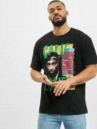 Camiseta de algodón negra con un gráfico central que presenta un diseño colorido y un retrato, texto en negrita en verde, amarillo y rojo. Corte estándar.