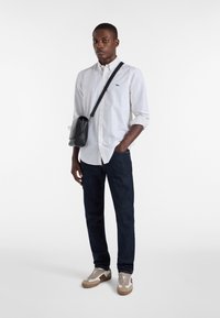 Biała koszula zapinana na guziki z małymi niebieskimi kropkami, w połączeniu z ciemnoniebieskimi dżinsami i beżowymi sneakersami. Czarna torebka na ramię o teksturowanym wykończeniu.