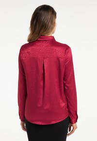 Rote Satinbluse mit strukturiertem Muster, geknöpften Manschetten und Kragen. Verfügt über eine Rückfalte und eine glatte, glänzende Oberfläche.