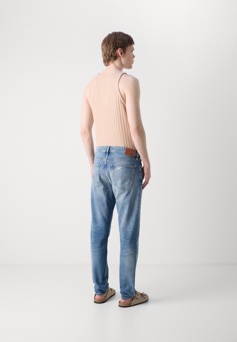 Hellrosa gerippter Tanktop kombiniert mit hellblauen Denim-Jeans, mit einem Lederlabel am Bund und flachen Sandalen.