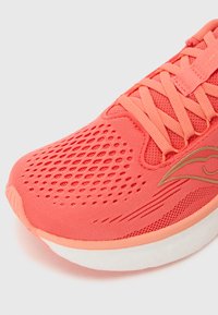 Chaussure de sport corail avec tige en mesh, superpositions texturées et semelle intermédiaire blanche. Équipée d'un système de laçage et d'un accent logo sur le côté.