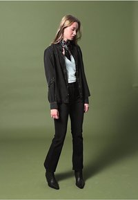 Giubbotto di denim nero con cuciture a contrasto, top bianco, jeans neri a vita alta e stivaletti neri. Sciarpa con decorazioni floreali.