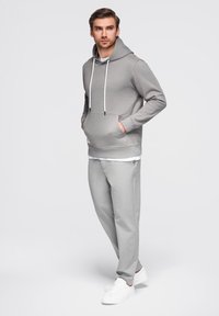 Šedá mikina s kapucí a bílými šňůrkami, přední kapsa; kombinováno s světle šedými kalhotami a bílými teniskami pro koordinovaný vzhled.