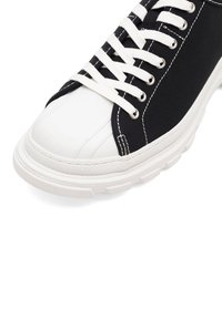 Czarne trampki na płaskiej podeszwie z białym czubkiem i białymi sznurowadłami oraz detalami w stębnowaniu. Posiadają teksturowaną podeszwę dla lepszej przyczepności.