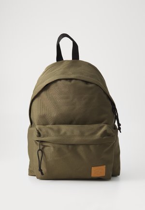 Mochila de tela verde oliva con forma redondeada, bolsillo frontal con cremallera y un parche de logo de cuero texturizado. Cuenta con correas y detalles en nylon negro.