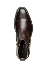 Bota de tobillo de cuero marrón con textura suave, acentos de doble hebilla, puntera redondeada y un interior acolchado. Logotipo de la marca visible en el interior.