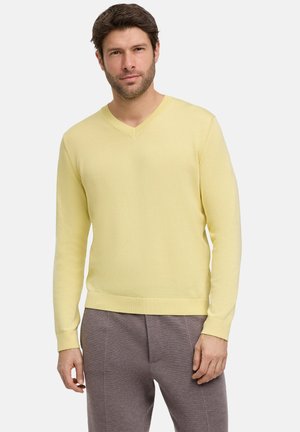 V-neck sweater in soft, light yellow knit fabric. Features long sleeves and a ribbed hem. Paired with gray, textured trousers.