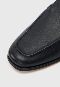 Μαύρο δερμάτινο παπούτσι με στρογγυλεμένη μύτη, ομαλή υφή και μινιμαλιστικό σχεδιασμό με διακριτική ραφή κατά μήκος των ακμών.