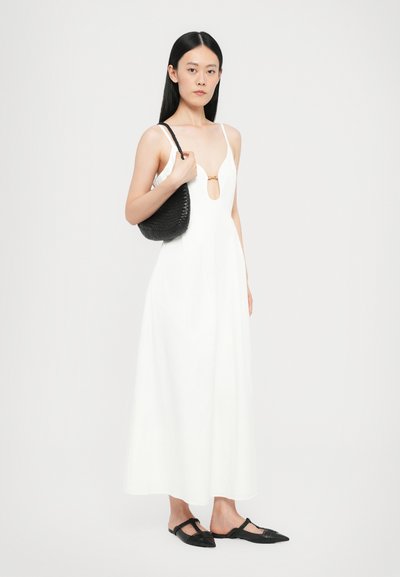 Vestido blanco sin mangas con un escote en forma de llave, dobladillo acampanado y textura suave. Un par de zapatos planos negros con punta y un bolso negro texturizado.