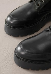 Czarne skórzane buty z połyskiem, z gruboziarnistą gumową podeszwą i kontrastującymi detalami w stichach po bokach.