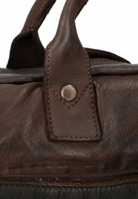 Borsa in pelle marrone caratterizzata da una texture liscia, dettagli cuciti e un'apertura metallica sul manico. Ingrandimento dell'attacco del manico.