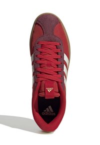 Röd sneaker med ovandel i mocka och textil, med vit tre-stripes design, röda snören och gummisula. Adidas-logotyp på tungan.