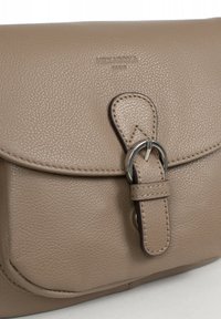 Borsa a mano in pelle beige con superficie texturizzata, dotata di chiusura a pattina, anello metallico e dettaglio cucito sulla tracolla. Logo del brand visibile.