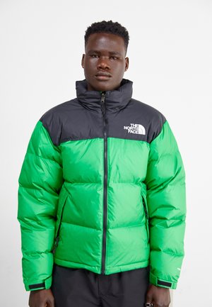Chaqueta acolchada verde y negra con un alto cuello, que cuenta con cierre de cremallera en la parte delantera, bolsillos laterales y un logo blanco en el pecho. Textura suave, diseño aislante.