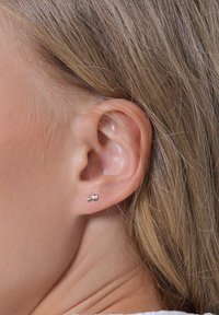 Srebrne češke naušnice s dva sferna oblika različitih veličina, pričvršćene u probijanju režnja. Glatka tekstura, minimalistički dizajn.