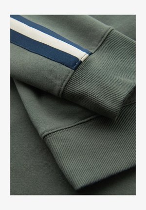 Manches repliées d'un sweat-shirt vert olive avec poignets côtelés, avec un détail rayé bleu et blanc sur une manche.