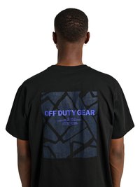 Personne portant un t-shirt noir avec un carré bleu à motifs et le texte « OFF DUTY GEAR » dans le dos, vue de dos sur fond blanc.