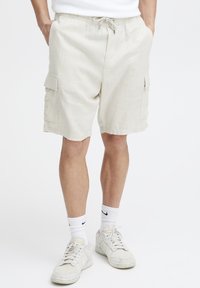 Beige cargoshorts van lichtgewicht stof, met zijzakken en een trekkoord in de taille. Gepaard met witte sokken en sneakers.