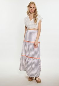 Fehér, textúrált mintájú cropped top, hosszú szoknyával párosítva, amely függőleges csíkokkal rendelkezik lila és narancssárga akcentussal. Espadrille szandál.
