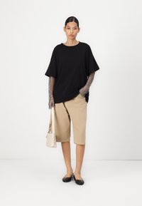 Černé oversized tričko s meshovými detaily na rukávech, khaki šortky do kolen a černé baleríny. Doplňěk: malá béžová kabelka.