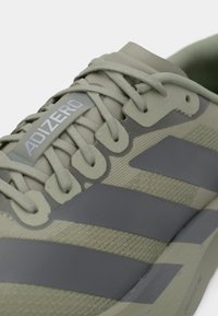 Κοντινό πλάνο γκρι αθλητικού παπουτσιού Adidas Adizero που δείχνει τα κορδόνια, τις θηλιές και τις τρεις σκούρες ρίγες στη υφασμάτινη, υφή επιφάνεια.