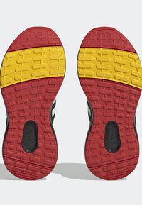Sole di scarpe atletiche nere con gomma testurizzata rossa e gialla e un motivo distintivo, contrassegnate con la dicitura "NON MARCANTE" sul lato.