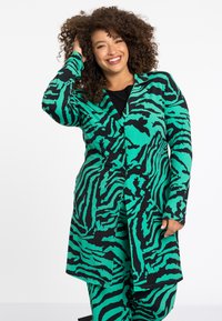 Groene en zwarte zebra-gepatroneerde lange jas met een knoopsluiting aan de voorkant, inkeping kraag en lange mouwen, gecombineerd met een zwarte top.