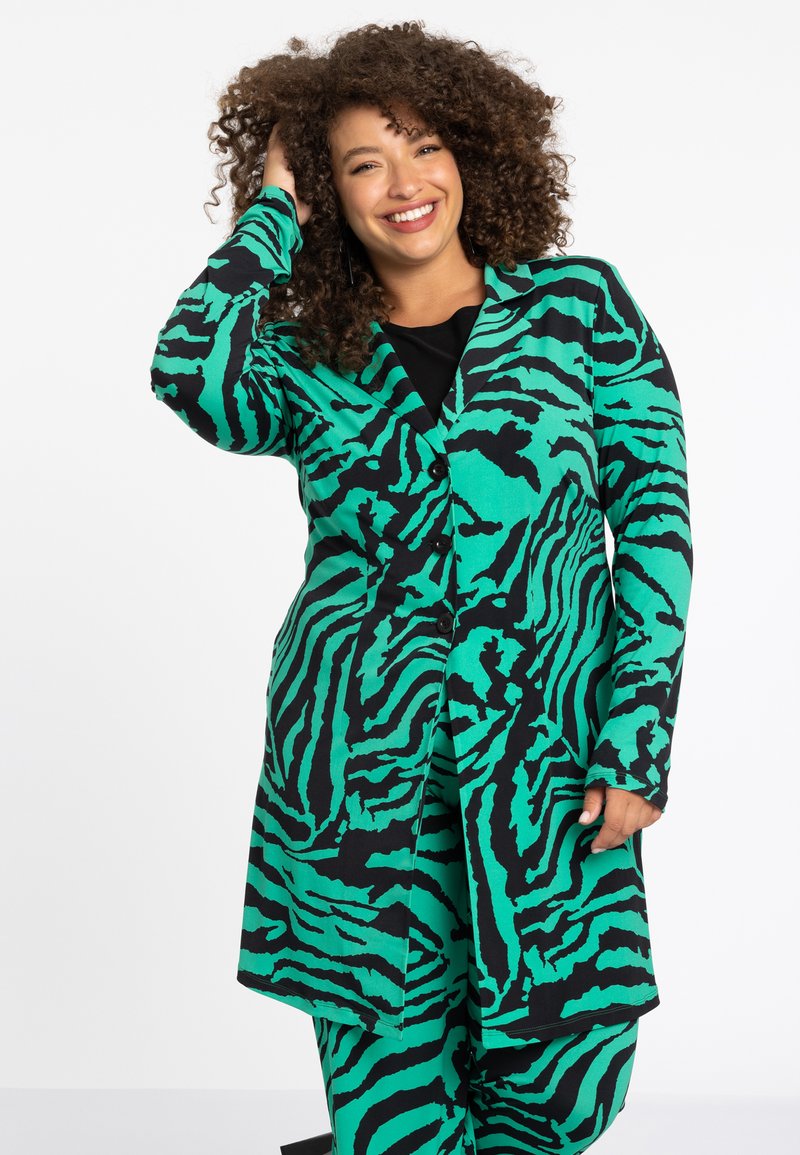 Groene en zwarte zebra-gepatroneerde lange jas met een knoopsluiting aan de voorkant, inkeping kraag en lange mouwen, gecombineerd met een zwarte top.