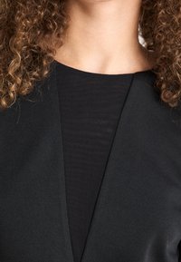 Černý top s výstřihem do V, s hladkou texturou a vrstvenou látkou. Má přiléhavý střih a elegantní vzhled.