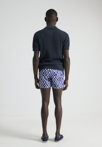 Polo de punto texturizado en azul marino combinado con pantalones cortos de rayas azules y blancas, visible desde la parte posterior. Calzado casual completa el conjunto.