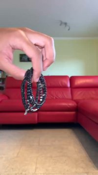 Svart flätade laddningskablar hålls i handen, med metalliska kontakter och en strukturerad yta, visas mot en röd soffa i bakgrunden.