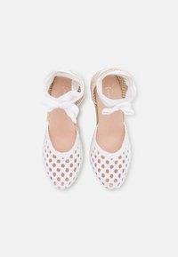 Espadrillas bianche in rete con un design a trama aperta, suole piatte e morbidi lacci in raso. L'interno presenta una soletta di colore beige chiaro.