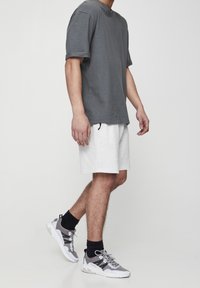 T-shirt gris à manches courtes, en tissu léger, associé à un short texturé blanc. Baskets grises et blanches avec des accents noirs, portées avec des chaussettes noires.