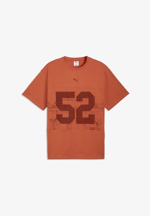 Kurzärmeliges T-Shirt in Rostfarbe mit dunkelroter "52" auf der Vorderseite und schwacher abstrakter Linienzeichnung hinter den Zahlen, Puma-Logo darüber.